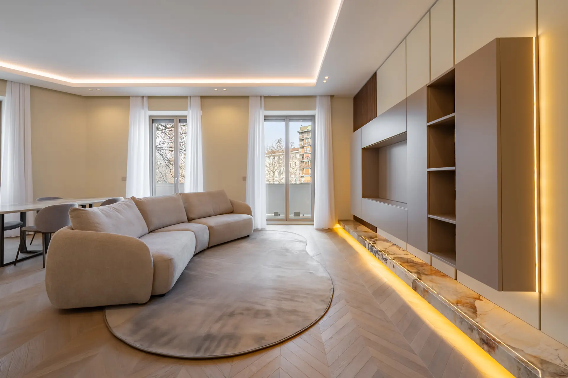 Soggiorno luminoso con divano curvo beige, parete attrezzata in onice retroilluminata e parquet a spina di pesce - Corso Sempione 15A Milano - Liberty House
